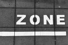 Een zwart-witfoto van straatsteen met de witte letters "ZONE" gemarkeerd op de grond.