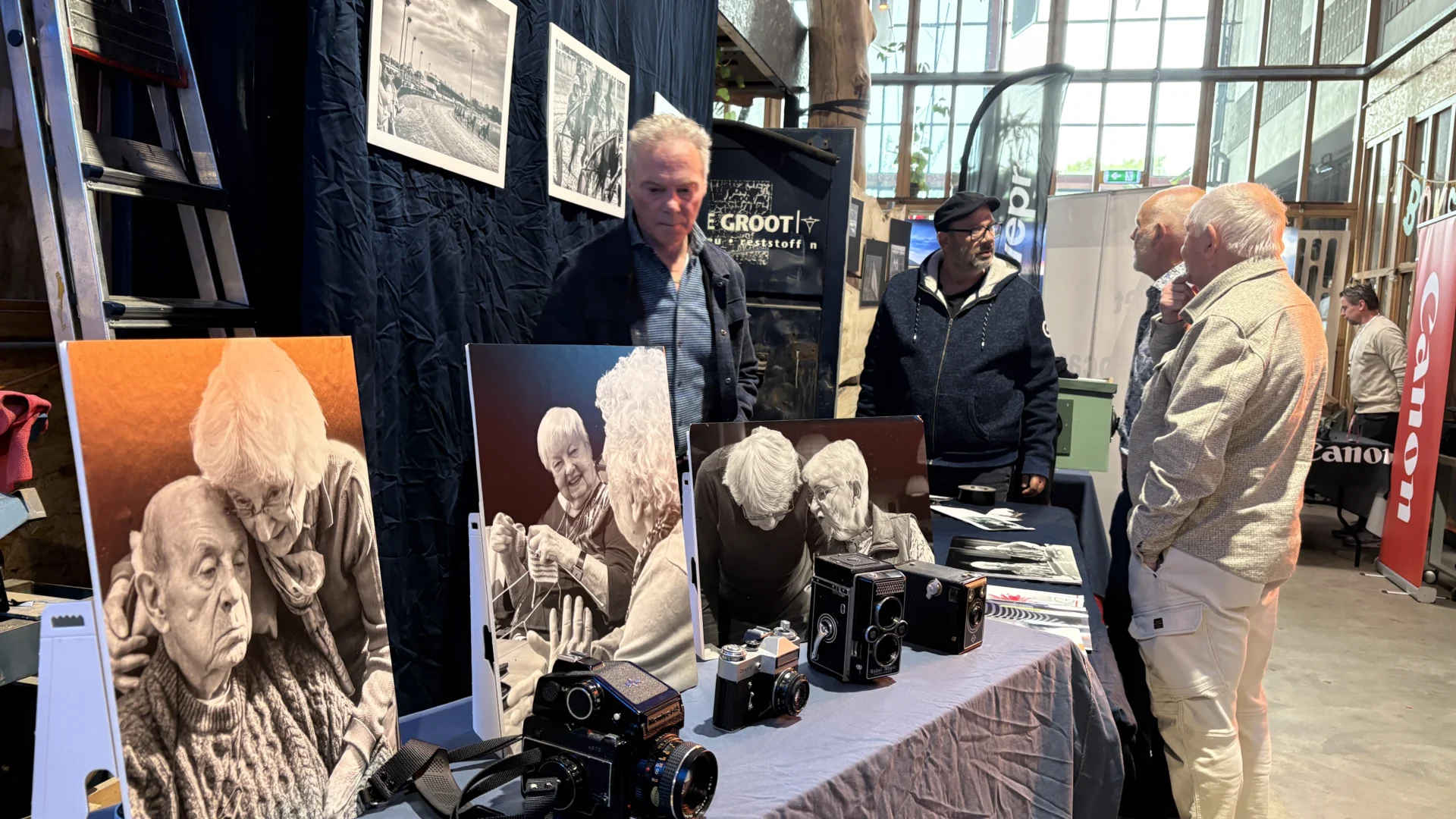 Beurstafel met oude camera's en foto's van ouderen, vijf mannen in gesprek.