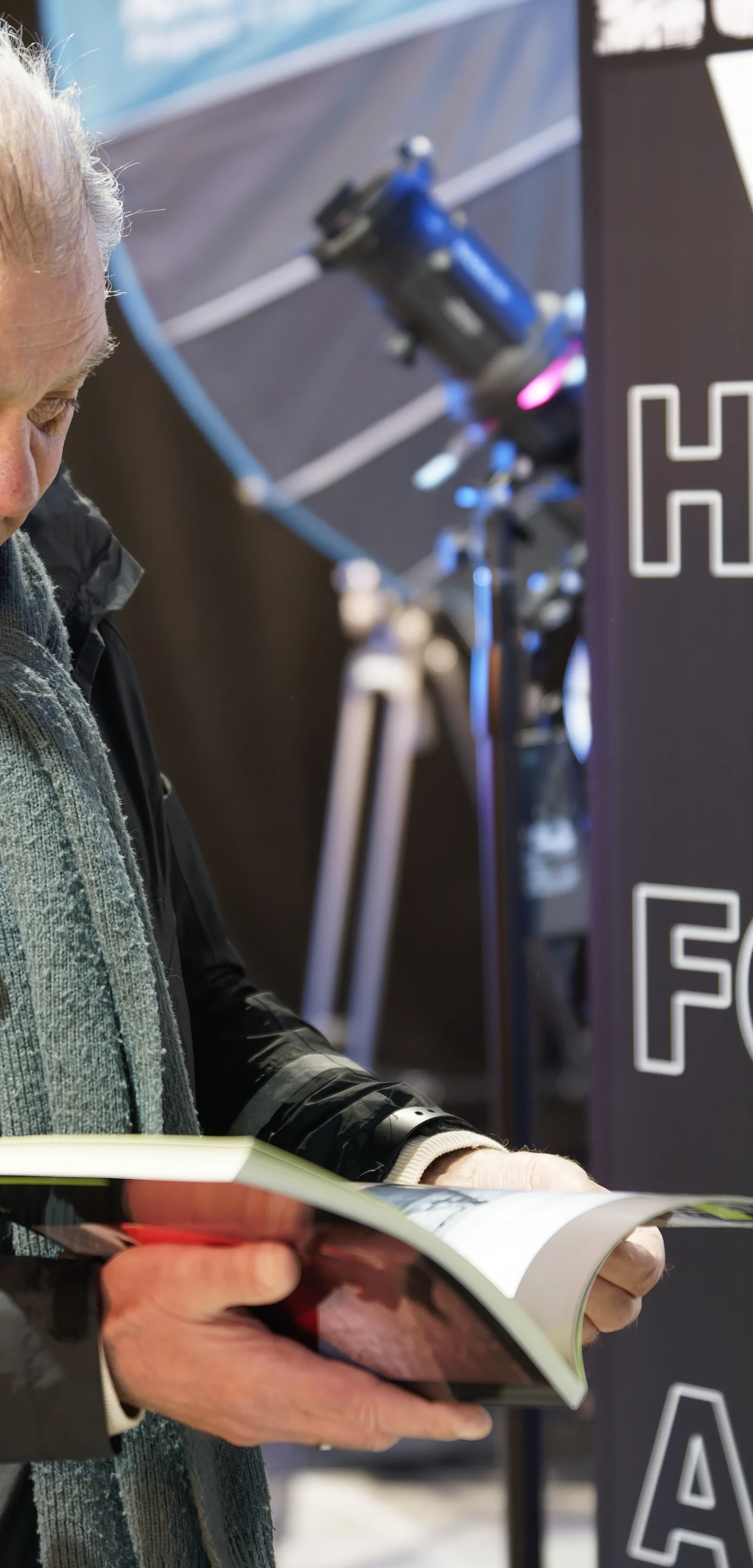 Twee oudere mannen bij een affiche Het Fotocafé Alkmaar, één bekijkt een boek.