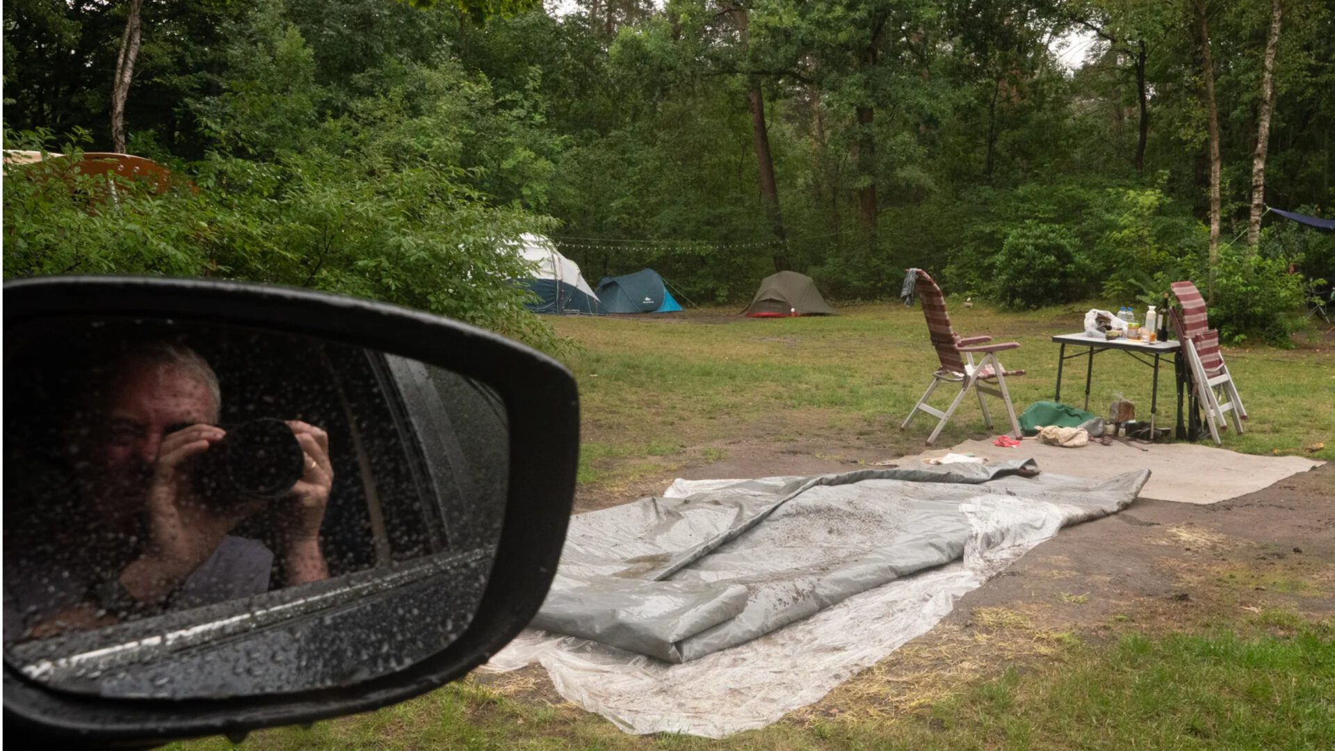Wim van Reenen Campingplek met plastic zeilen, campingstoelen en tenten in een bosrijke omgeving.