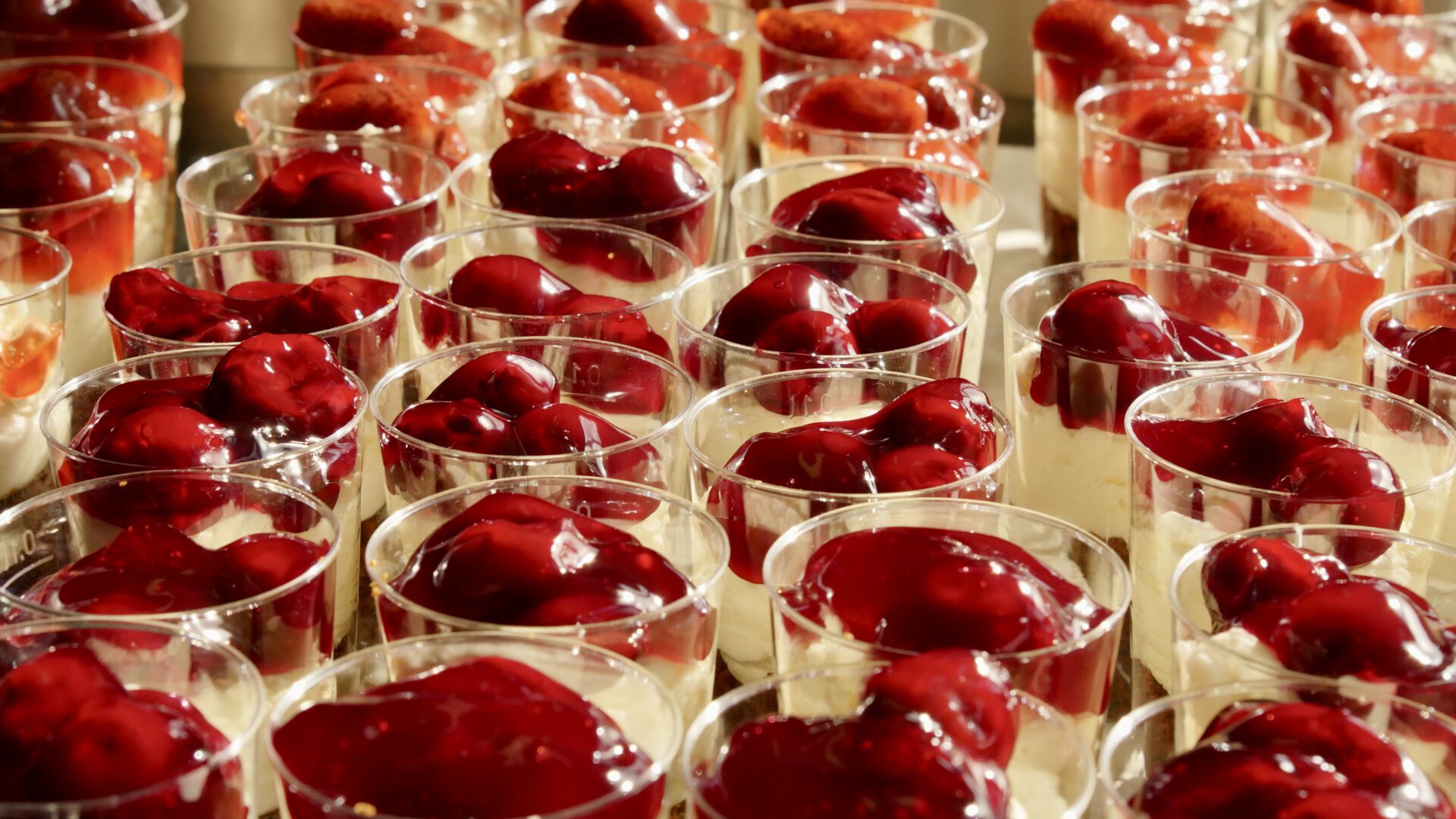 Glazen met witte crème, bedekt met kersen- en aardbeiensaus.